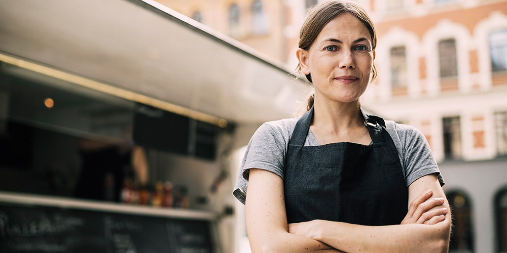 Vooraanzicht van zelfverzekerde, vrouwelijke chef-kok die voor een voedseltruck in de stad staat Vooraanzicht van zelfverzekerde, vrouwelijke chef-kok die voor een voedseltruck in de stad staat